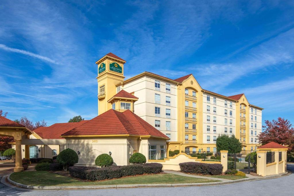 Hotel with a cream exterior and red-tiled roofs, featuring a tower and manicured shrubs under a clear blue sky.