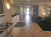 Hotel lobby with tiled floor, reception desk on the left, and seating area with two striped armchairs on the right. A door at the end of the hallway leads outside.