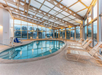 Indoor swimming pool with a curved shape, surrounded by lounge chairs and enclosed by large glass windows.