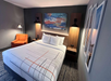 Hotel room with a neatly made bed, orange chair, two lamps, and abstract artwork on the wall.