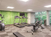A gym with two treadmills, an exercise bike, and a weight bench. Large windows and a green motivational wall are visible.
