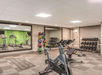 A modern gym with exercise bikes, free weights, colorful medicine balls, and a wall mirror. Tables and motivational green wall are visible in the background.