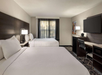 Hotel room with two double beds, a desk and chair, wall-mounted TV, and a window with curtains.