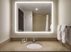 A bathroom counter with a sink, illuminated mirror, and towels on a rack. Toiletries are neatly arranged next to the faucet.