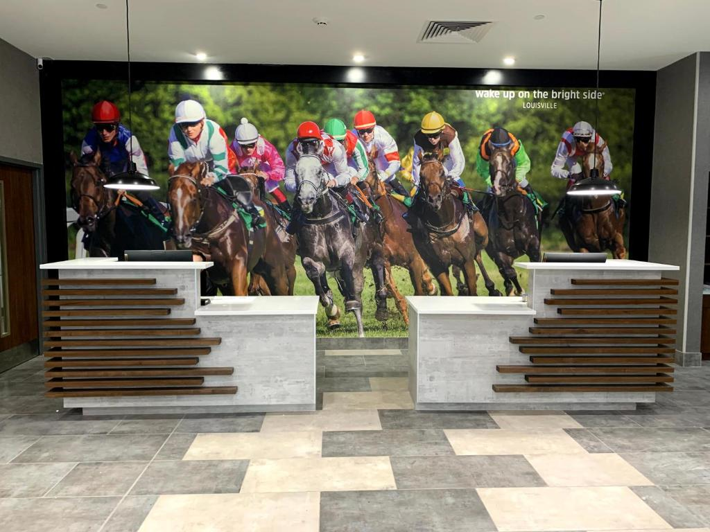 Two modern reception desks sit in front of a large wall mural depicting a horse race with jockeys in colorful uniforms.