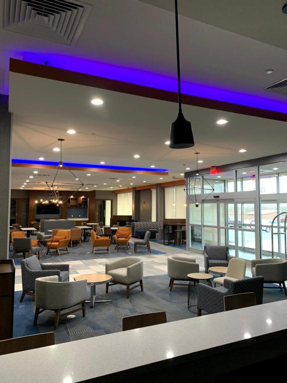 Modern hotel lobby with various seating areas, armchairs, and tables, illuminated by ceiling lights and purple accent lighting, with large windows at the entrance.