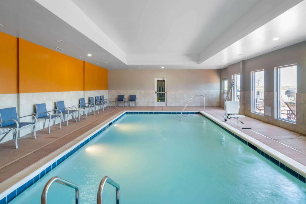 Indoor swimming pool with clear water, surrounded by blue chairs along one wall and large windows letting in natural light.