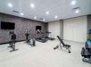 A modern gym room with two treadmills, an exercise bike, a weight bench, dumbbells, medicine balls, and two wall-mounted TVs.