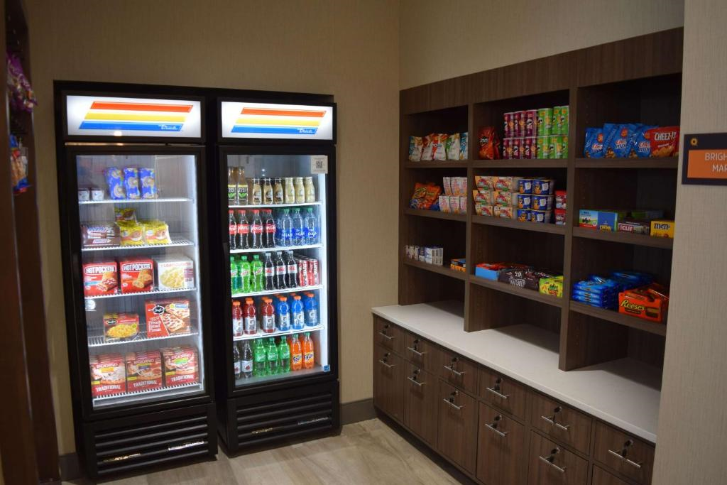 Small convenience store corner with two refrigerated display cases stocked with drinks and snacks, and adjacent shelves holding various packaged snacks.
