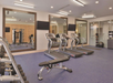 A gym with treadmills, weight benches, dumbbells, exercise balls, and a multi-exercise machine. Mirrors and wall-mounted TVs are visible.