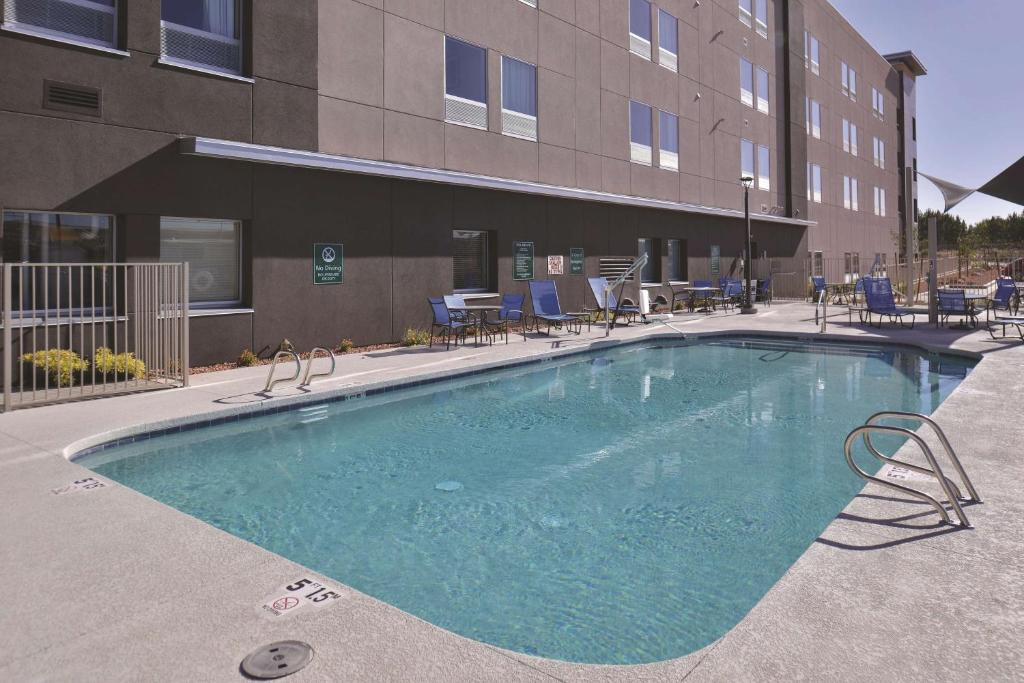 Outdoor swimming pool next to a modern hotel building, surrounded by chairs and tables.