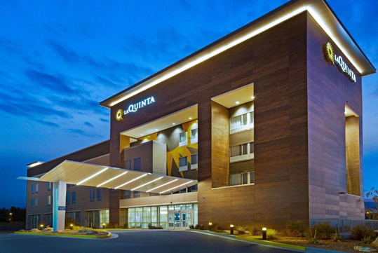 Modern hotel building with a lit exterior, featuring large windows and a covered entrance, against a twilight sky.