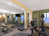 A gym room with treadmills, ellipticals, and exercise mats. Large mirrors cover one wall.