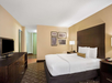Hotel room with a large bed, dark wood furniture, a flat-screen TV, and framed artwork on the wall. Carpeted floor and beige walls create a neutral ambiance.