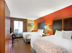 Hotel room with two double beds, colorful accent wall, a desk with a chair, and a window with striped curtains.