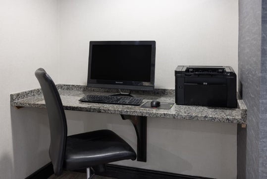 A small office corner with a desktop computer, keyboard, mouse, and a printer on a granite countertop, next to a black office chair.