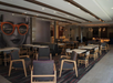 Modern hotel lounge with wooden chairs, tables, and a large poster of a person wearing orange sunglasses on the wall.