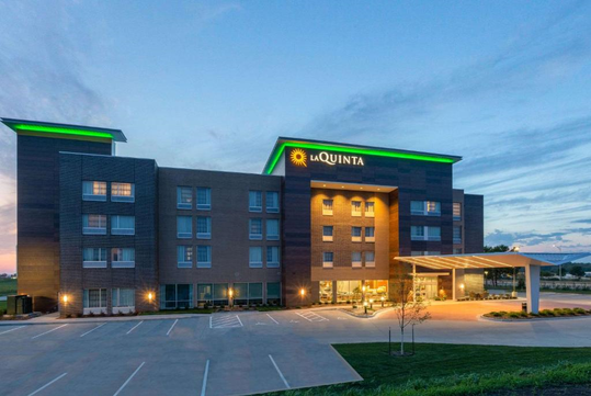Exterior of a four-story La Quinta hotel with illuminated signs, modern design, large glass entrance, and an empty parking lot at dusk.
