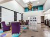 A sitting area with gray and purple chairs and small coffee tables across from the dark wooden front desk at the La Quinta by Wyndham New Braunfels.