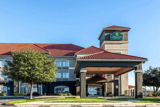 The front covered entrance of the La Quinta by Wyndham with trees on both sides on a bright sunny day in New Braunfels, Texas.