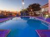 An outdoor swimming pool with deep blue water and lounge chairs lining the sides at sunset at the La Quinta by Wyndham New Braunfels.