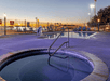 An outdoor hot tub with a swimming pool behind it and lounge chairs lining the sides at sunset at the La Quinta by Wyndham New Braunfels.