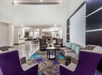 A lounge area with gray and purple chairs, gray couch, coffee table, and a gray and purple carpet with a breakfast bar in the background.
