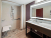 Accessible bathroom with a roll-in shower, grab bars, and a shower chair. A large mirror and sink with toiletries are on the right, set against a purple accent wall.