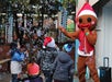 A person in a gingerbread costume and red hat entertains a group of children in winter clothing surrounded by floating bubbles outdoors.