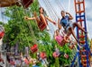 Several riders enjoying the thrill as they swing outward on a carousel under a clear sky with scattered clouds and lush green trees in the background.