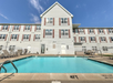 Outdoor swimming pool in front of a three-story white building with multiple windows.