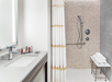 Modern bathroom with a sink, mirror, toiletries, and a walk-in shower. Towels are stacked on a white bench beside the shower.