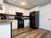 Modern kitchen with white cabinets, black appliances, wood-patterned flooring, and a mix of countertop appliances and utensils on the counters.