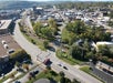 Aerial view of a small city with intersecting roads, railroad tracks, commercial buildings, trees, and parked vehicles on a clear day.