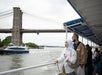 People on a ferry ride enjoy the view of the Brooklyn Bridge and a boat passing by on the river.
