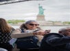 A woman in sunglasses takes a selfie on a boat with the Statue of Liberty in the background.