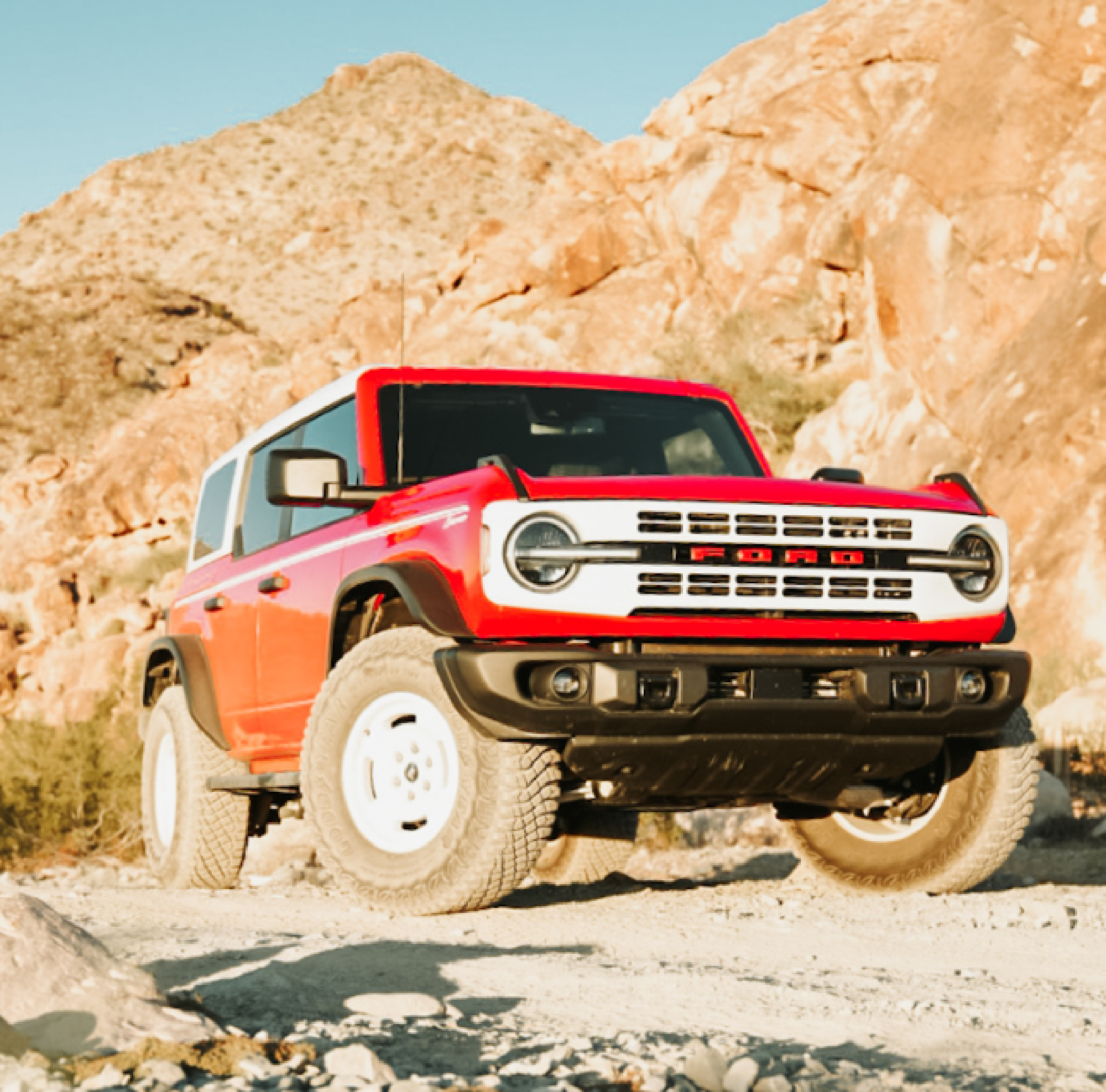 A red and white off-road vehicle is parked on a rocky dirt path in a desert landscape with mountains in the background.