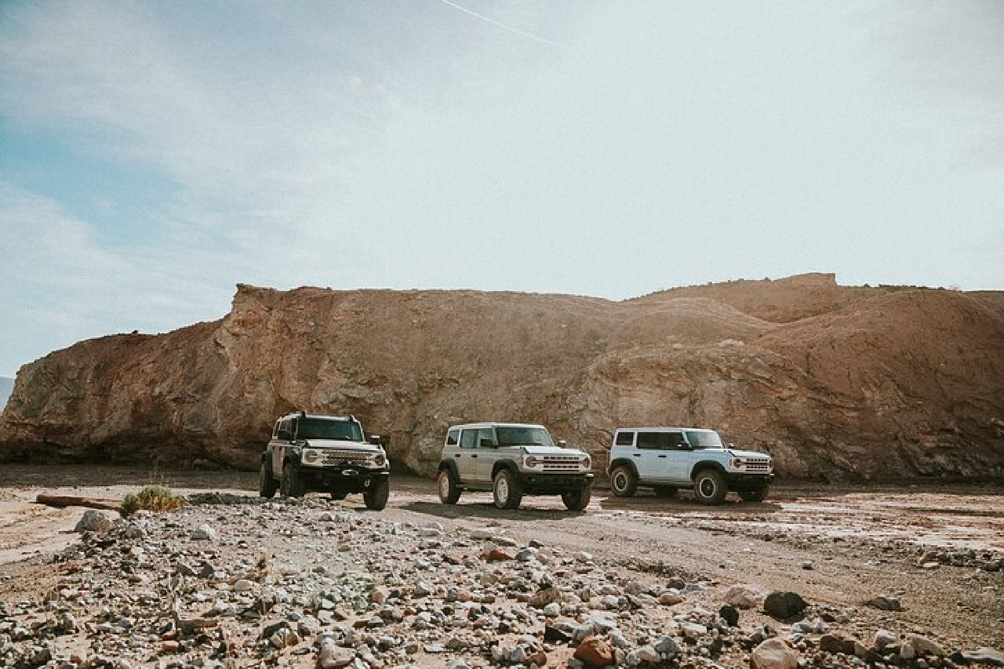 Three SUVs parked on a rocky desert terrain with a backdrop of large sand-colored rock formations under a clear sky.