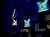 A woman with long dark hair in a white and black baseball t-shirt performing on stage at the Las Vegas Live Comedy Club.