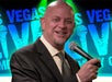 A bald man in a suit holding a microphone and performing on stage at the Las Vegas Live Comedy Club.