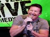 A man in a gray t-shirt holding a microphone and laughing on stage at the Las Vegas Live Comedy Club in Las Vegas, NV.