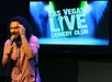 A man with long curly hair wearing a hoodie performing on stage at the Las Vegas Live Comedy Club.