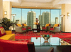 A large lobby decorated in red and yellow with ample cushioned seating and a large window showing city buildings on a sunny day.