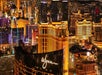 Aerial view of a Maverick helicopter flying over the Las Vegas strip at night with golden hotel lights illuminating the city.