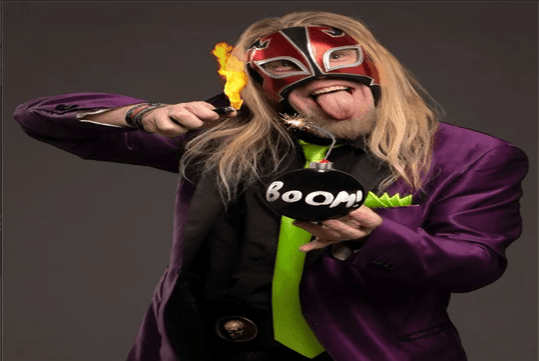 The Shocker in a purple and green suit performing a trick with a fake bomb with the fuze lit in his hand at the Late Night Magic Las Vegas.