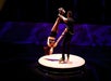 Two performers on roller skates execute an acrobatic move on a circular platform, with one holding the other's legs as she hangs upside down.