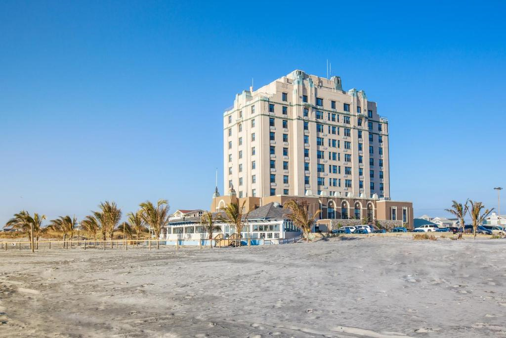 A tall, multi-story building stands on a sandy beach with palm trees and a clear blue sky in the background.