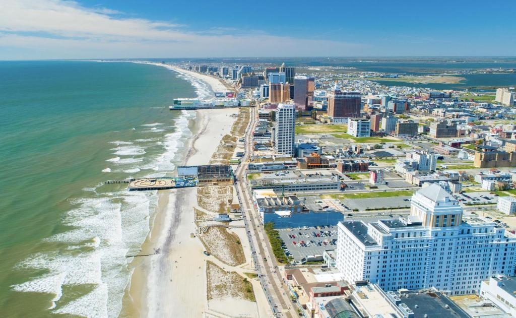 Aerial view of a coastal city with a sandy beach, ocean waves, and numerous buildings including hotels and casinos along the shoreline. A pier extends over the water.