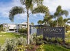 Legacy Vacation Resorts entrance with a sign and palm trees, surrounded by landscaped greenery. A modern building is in the background under a blue sky.