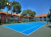 Blue tennis court outdoors surrounded by trees and red-roofed buildings under a clear blue sky.